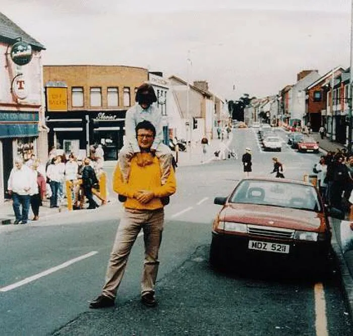 A man with a person on his shoulders in the middle of a street, an unsettling photo from daily life.