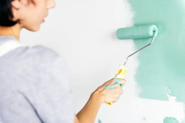 A person painting a wall light green, a metaphor for changing harmless habits in their 20s.