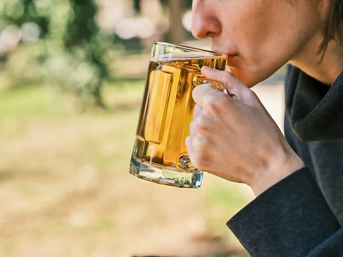 A person in their 20s drinks beer from a mug, symbolizing potentially destructive habits.
