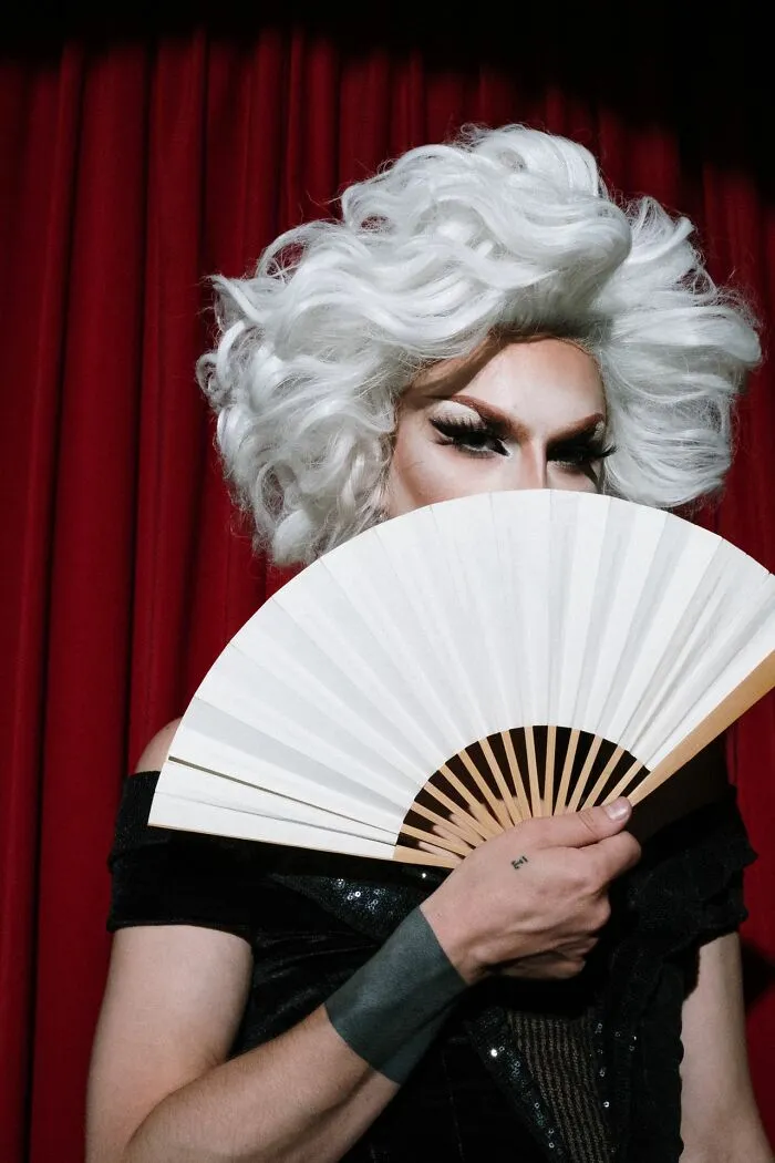 A person in a white wig and makeup holding a fan, depicting women shutting down creepy men.