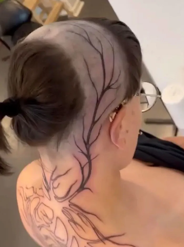 A unique hairstyle featuring a tree branch design shaved into the side of a person's head, revealing a bold and artistic look.