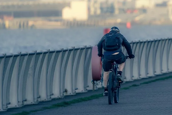 A cyclist riding along a paved path next to a body of water, an absurd yet common sight for daily commuters.