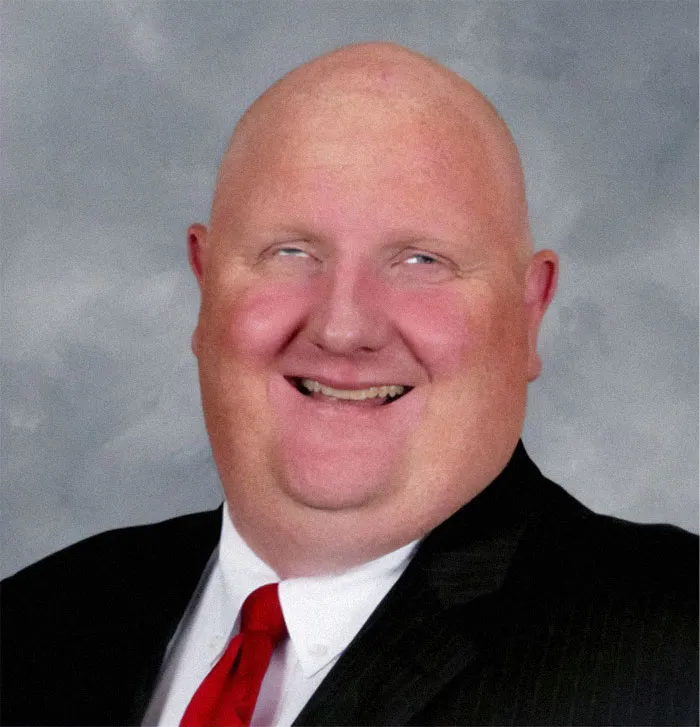 A bald man with a red tie smiling, from the not interesting community photos.