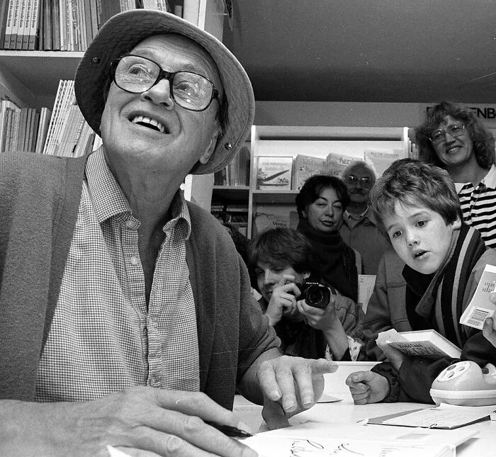 An older man in glasses and a hat signing autographs for a crowd, setting amazing world records.