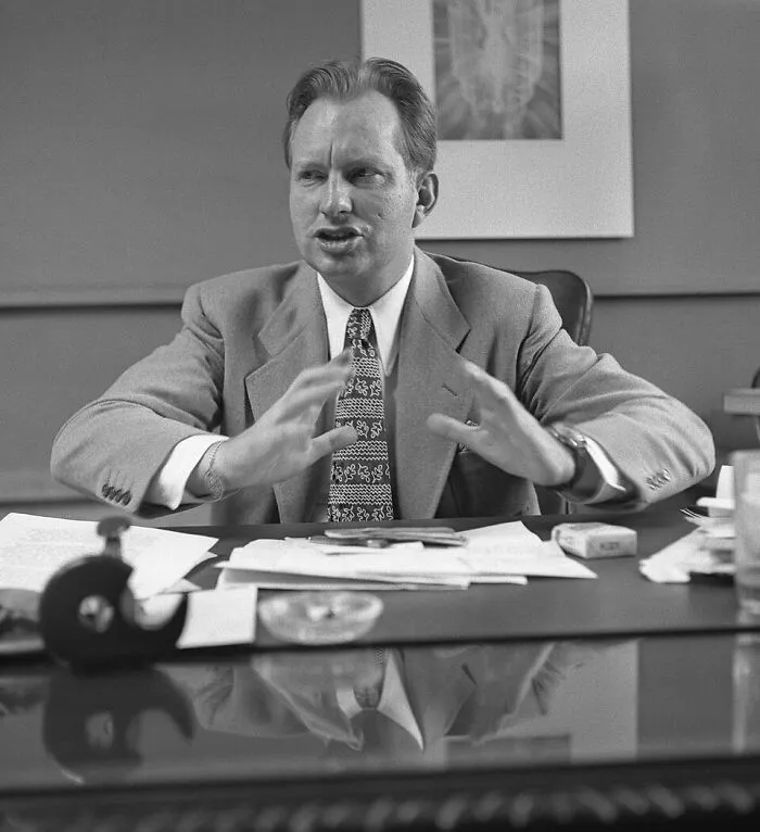 A black and white image of a man gesturing at a desk, a figure from incredible world records throughout history.