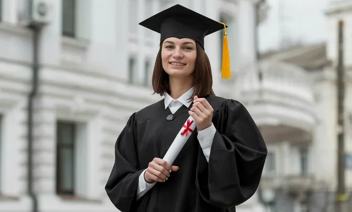 A smiling graduate in a cap and gown, holding a diploma, a real deal of her hard work and a sign from the universe.