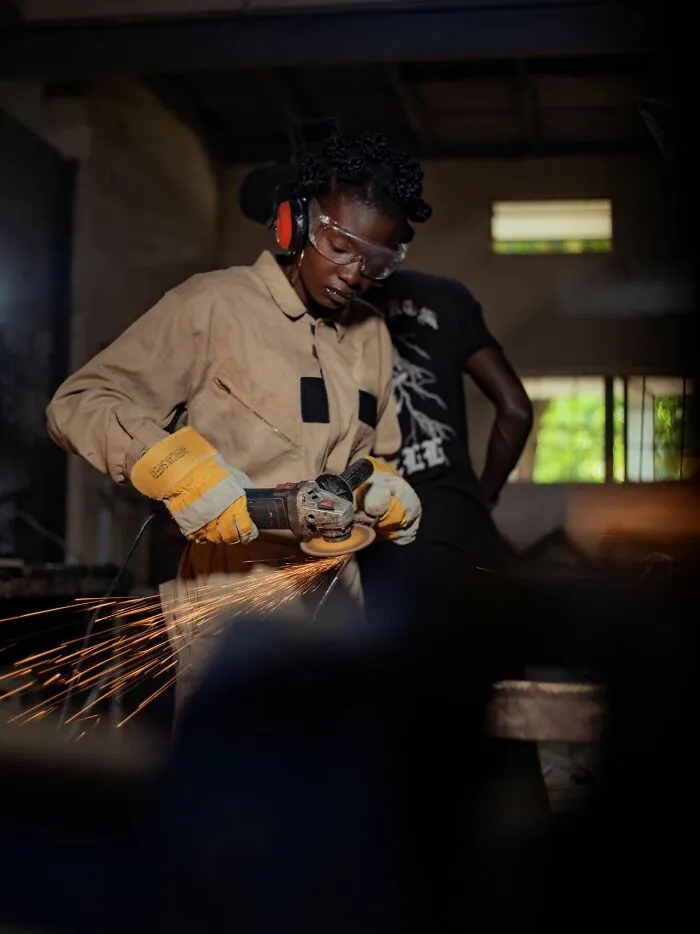 A woman wearing safety gear uses a power tool, challenging gender roles and toxic femininity.