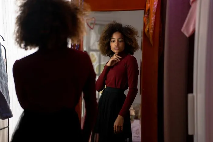 A young woman looking at her reflection in a mirror, contemplating societal gender roles and toxic femininity.