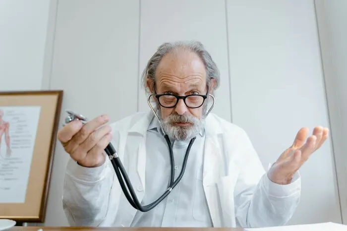 An older medical field worker shrugging with a stethoscope, conveying the challenges and frustrations medical workers encounter.
