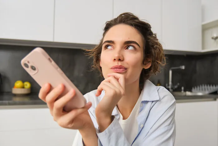 A thoughtful woman holding a smartphone, contemplating a sign from the universe and how to make real deals.