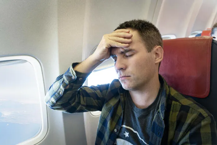 A man with a headache sitting in a plane seatmate position by the window, looking stressed