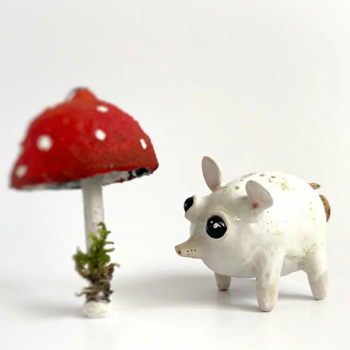 Small white pig-like weird ceramic sculptures next to a red mushroom as home decor