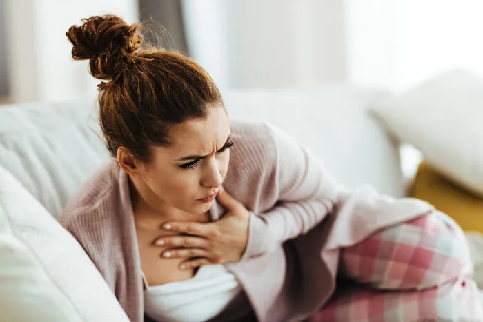 A young female patient holding her chest in pain while sitting on a couch