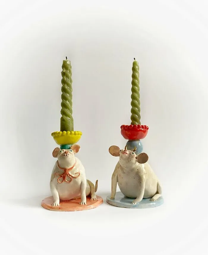 Two weird ceramic sculptures of chubby pig-like creatures holding candles on their heads.