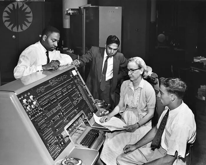Grace Hopper, a leading woman in computer science and Women In History, working with a large computer and male colleagues.
