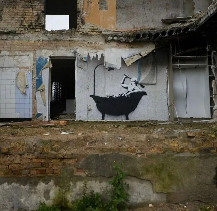 An abandoned building with powerful street art depicting a figure in a bathtub amidst the ruins.