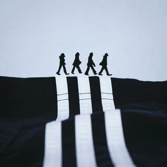 Playful illustrations featuring silhouettes walking on the white stripes of a black fabric track jacket