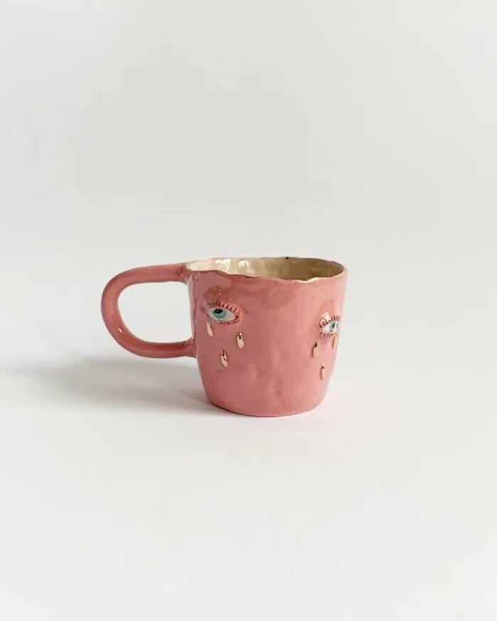A pink ceramic mug with crying eyes, showcasing weird ceramic sculptures for home decor