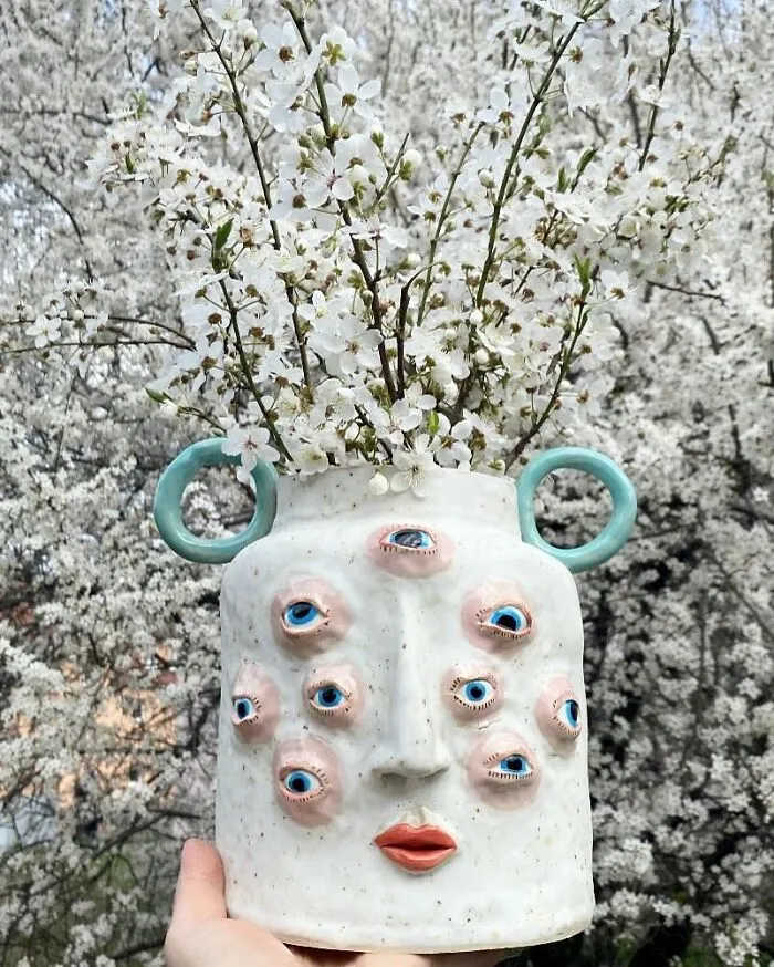 Weird ceramic sculptures vase with multiple blue eyes holding white flowers as home decor