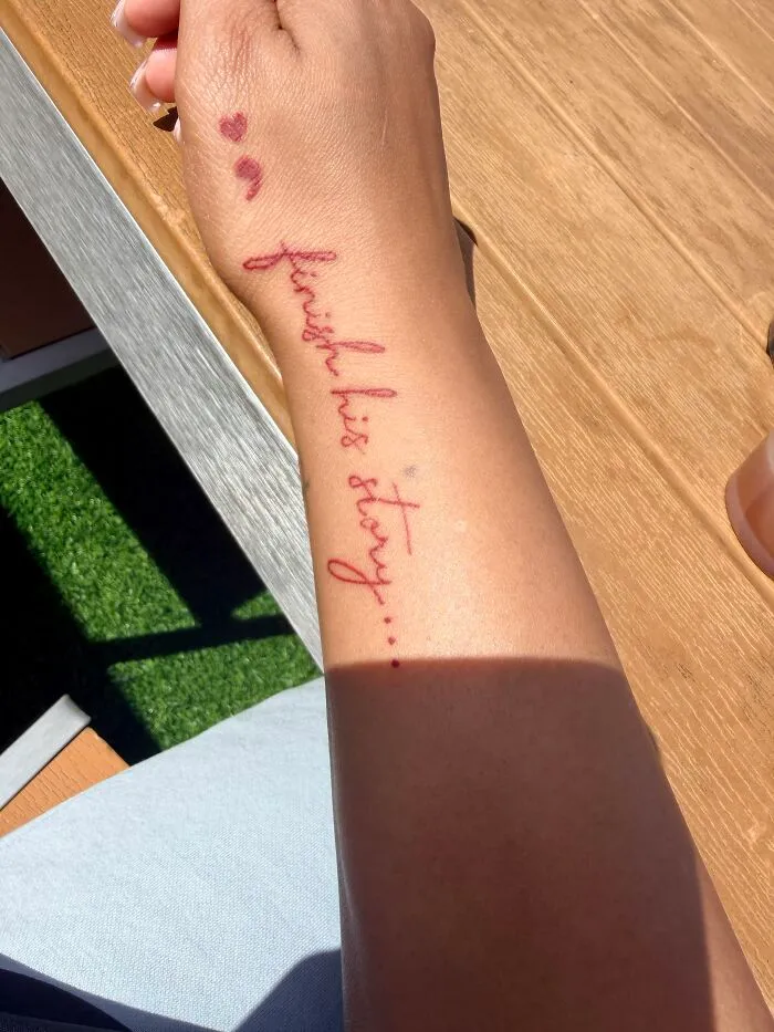 A forearm with a red script tattoo that reads finish his story... alongside three small red heart tattoos. These tattoos might break your heart.