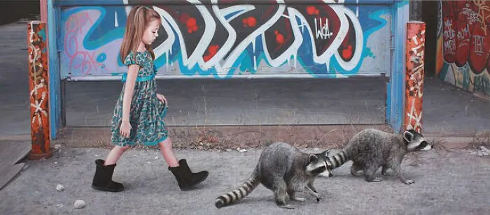 A young girl walks alongside two raccoons on a city street from dystopian paintings by Kevin Peterson.