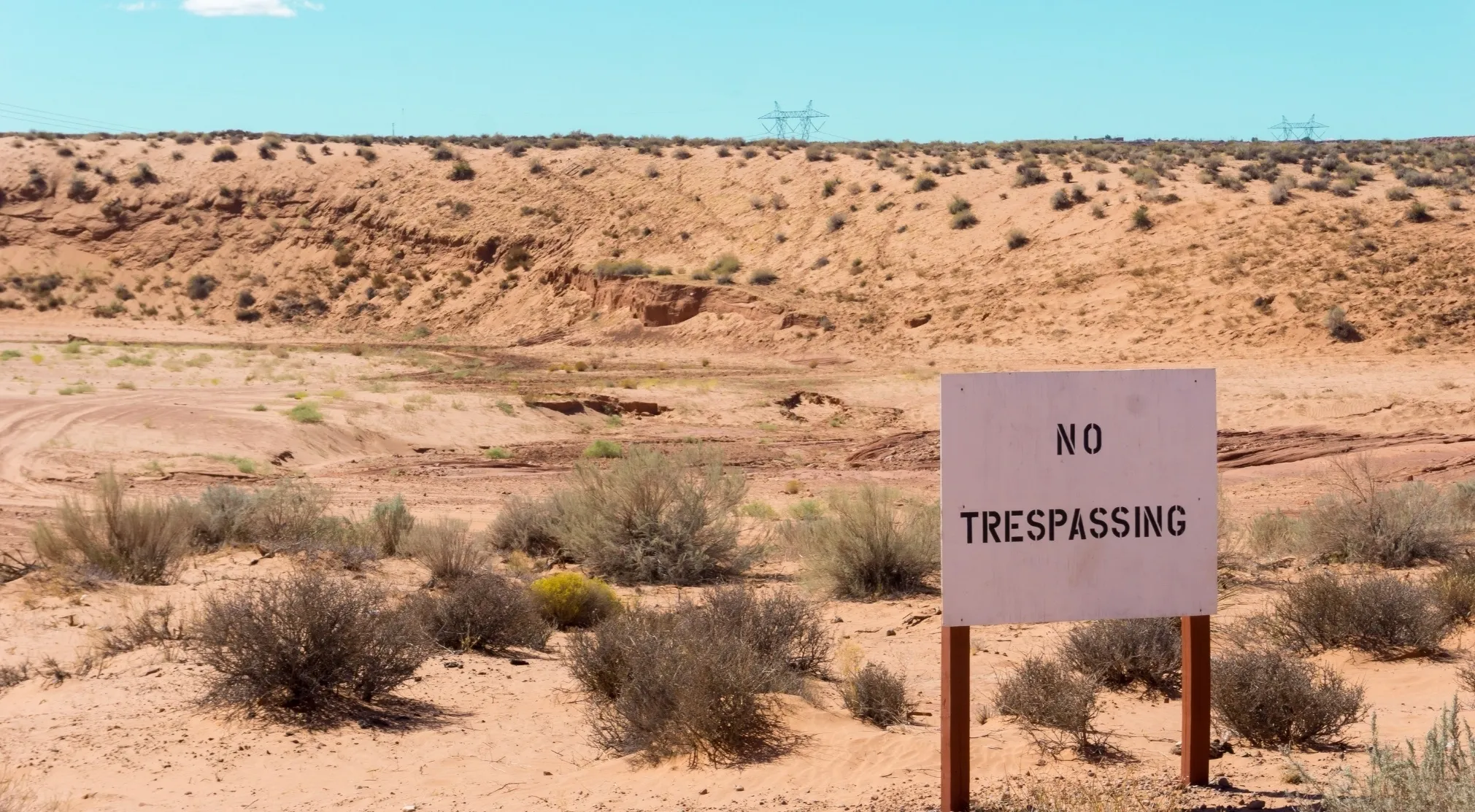 A NO TRESPASSING sign in a barren, sandy landscape with desert shrubs, hinting at the remote location of AREA 51 and UFO conspiracy theories.