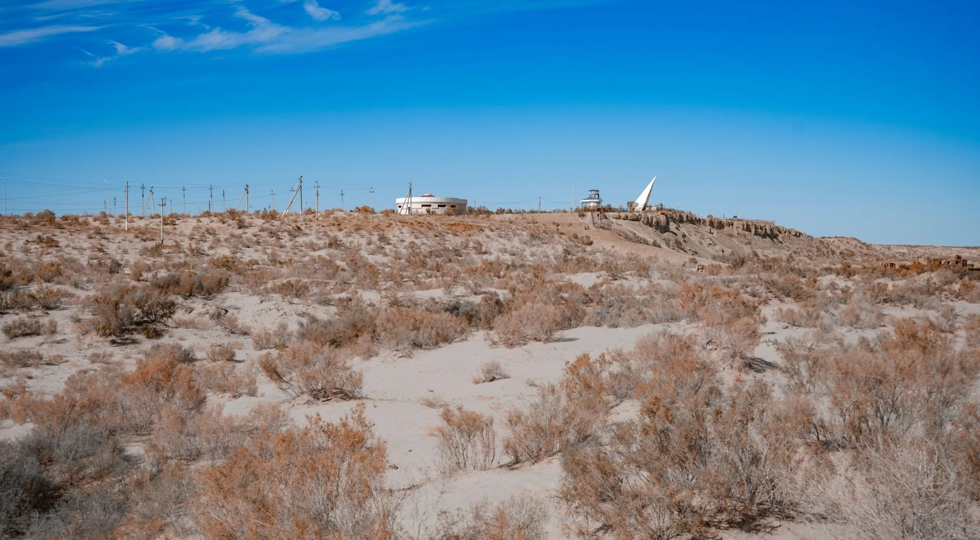 Desert landscape with buildings on a distant ridge, hinting at a hidden base linked to UFO and conspiracy theories.
