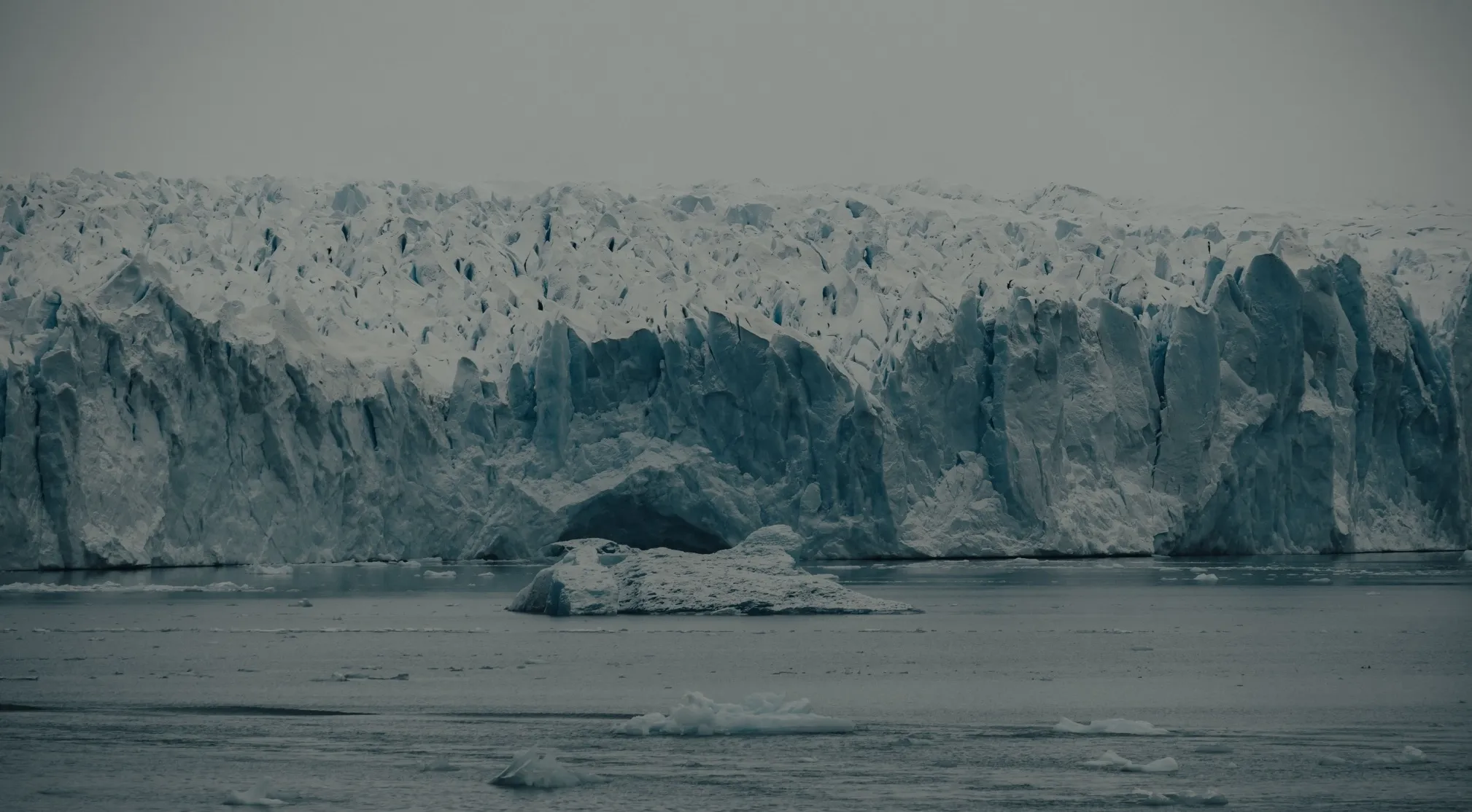 Massive icy glacier looming over dark water with small icebergs. UFO and conspiracy theories connect Antarctica to secrets.