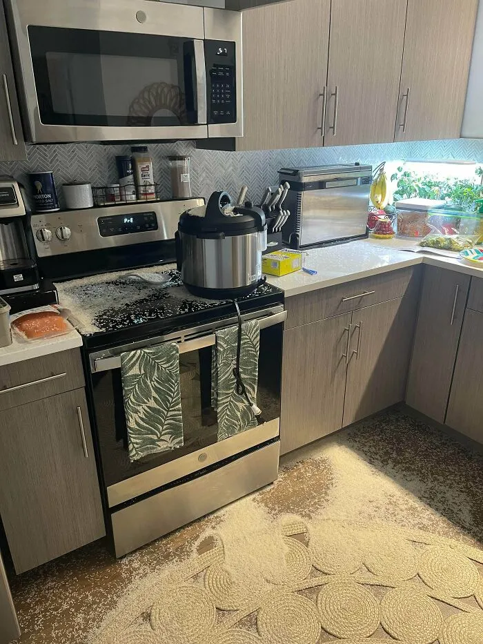 A modern kitchen with a large explosion of white contents on the stove, floor, and counters, a major kitchen fail.