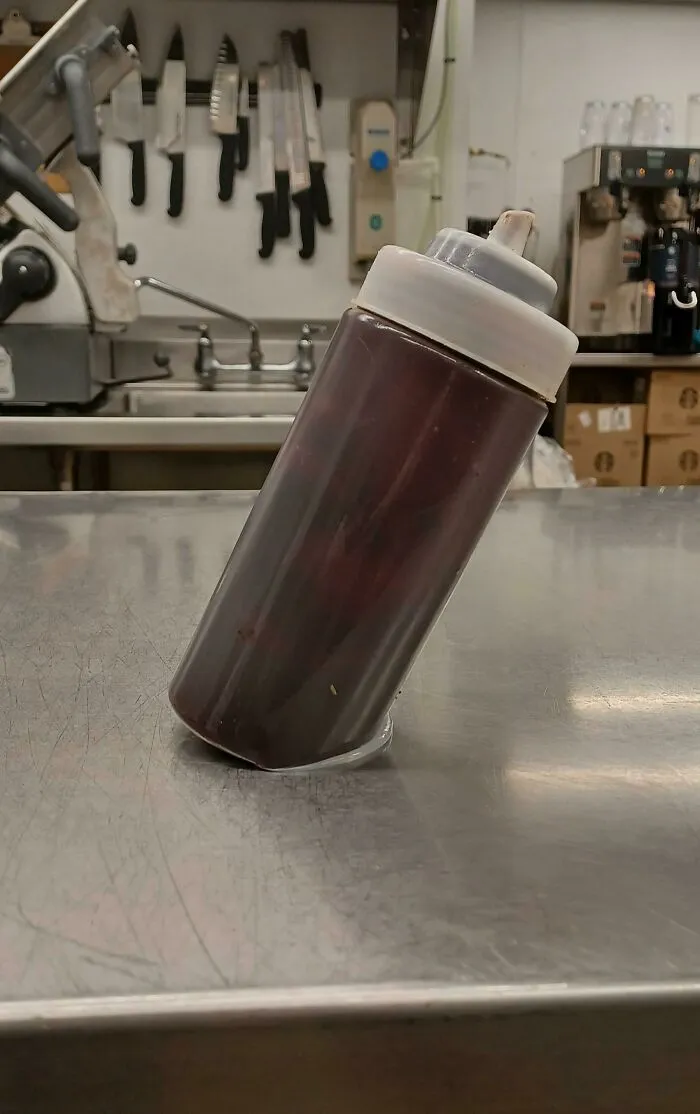 Squeeze bottle filled with dark liquid precariously balanced on a stainless steel counter, a kitchen fail waiting to happen.