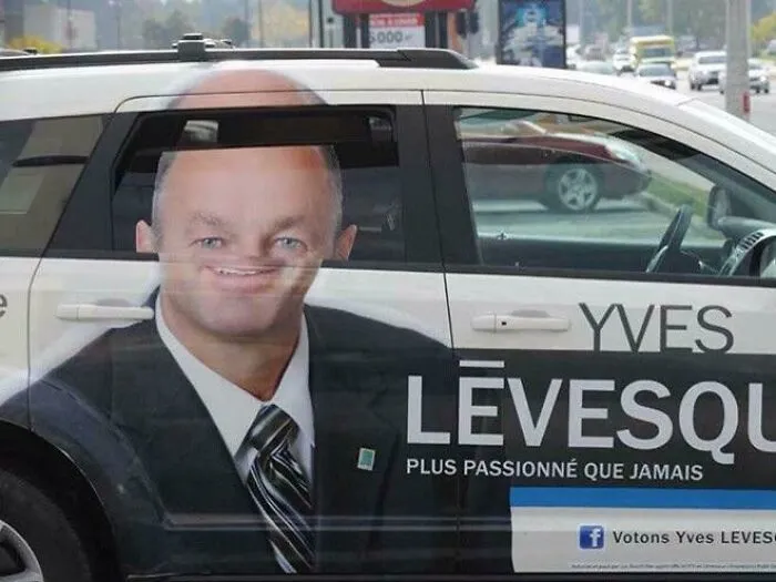 A hilarious ad placement on a car for Yves Lévesque, where the window creates a distorted, funny smile on his face.