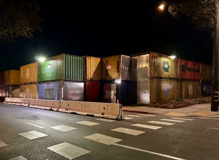 Stacked shipping containers at night with concrete barriers, representing the horrid and sad world.