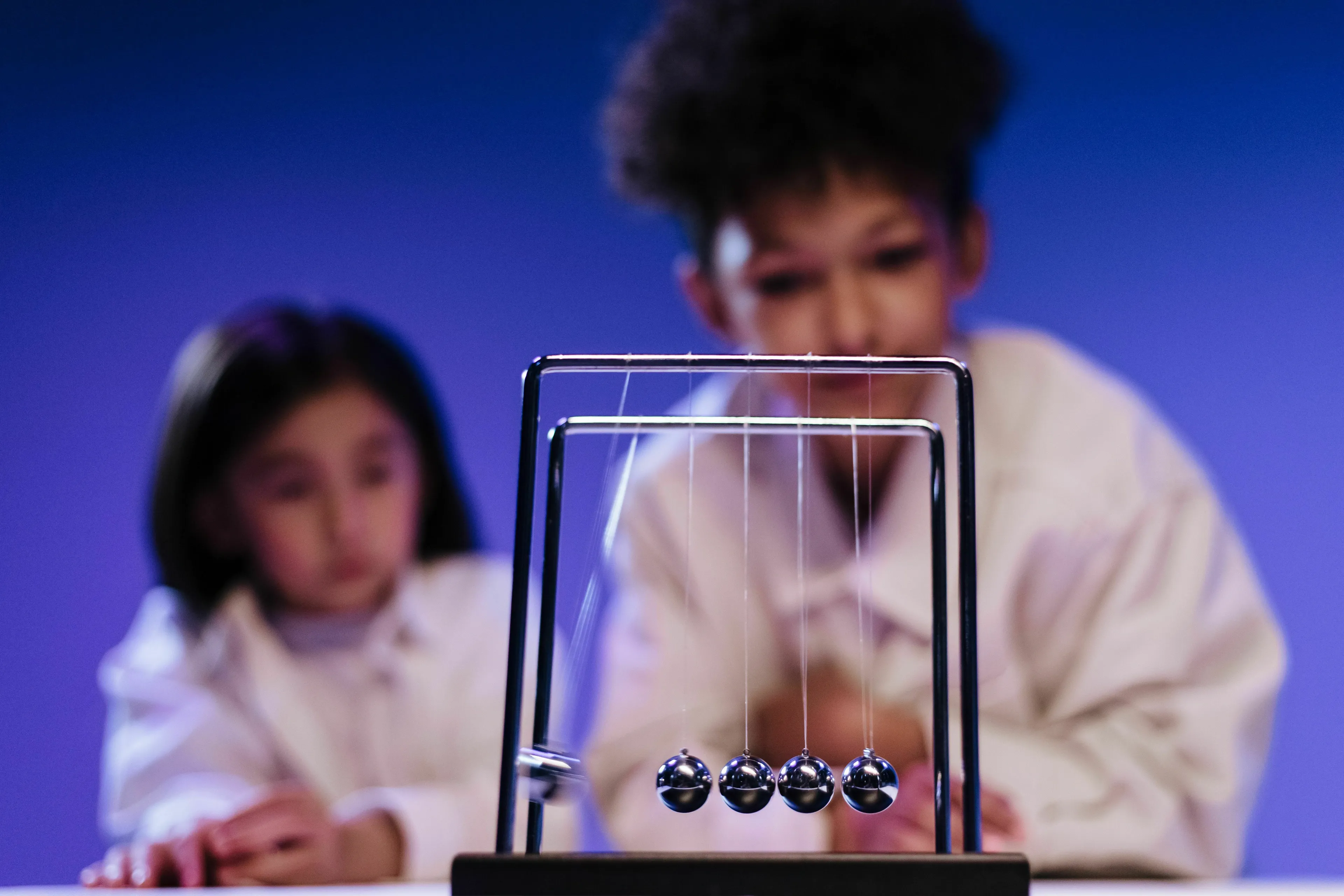Two children observing a Newtons Cradle, related to a General Knowledge Quiz on physics.