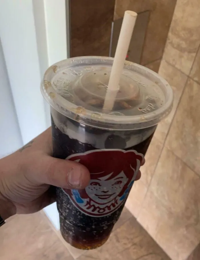 A hand holding a Wendy's soda cup, showing a horrid and sad world.
