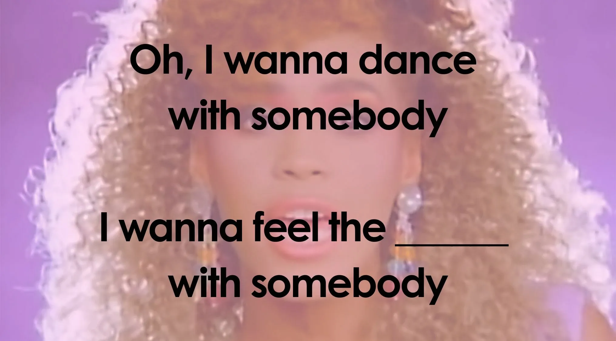 A female singer with curly hair on stage with the lyrics Oh, I wanna dance with somebody I wanna feel the___ with somebody for a Finish The Lyrics Quiz.
