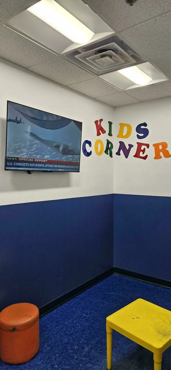 A TV in a Kids Corner displaying a news report about a military attack, portraying a dystopian American Dream.