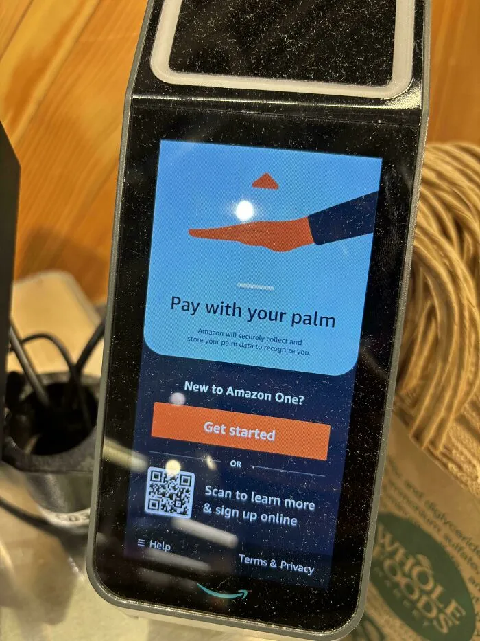 A close-up of an Amazon One device displaying 'Pay with your palm,' highlighting the dystopian nightmare of biometric payment.