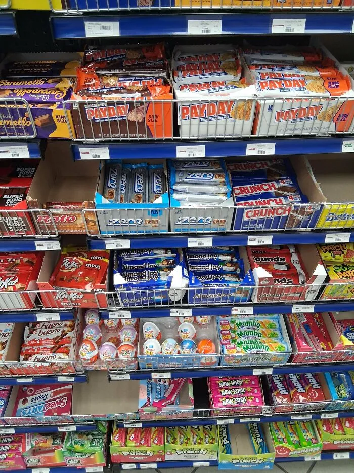 A supermarket aisle filled with various candy bars and snacks, showing the American dream of abundance.