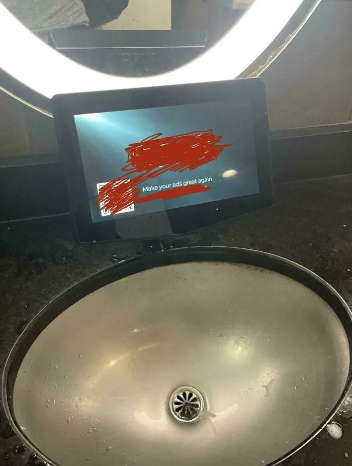 A tablet in a public restroom displaying 'Make your ads great again,' a dystopian nightmare of pervasive advertising.