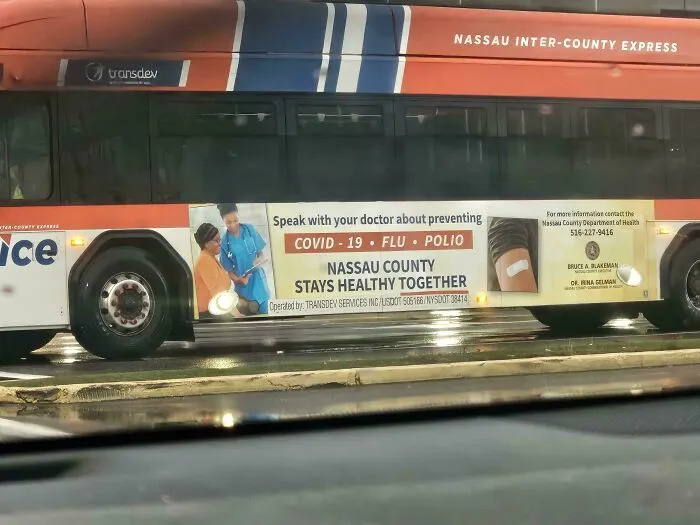 A bus with an advertisement for Nassau County about preventing COVID-19, flu, and polio, showcasing a dystopian nightmare of public health.