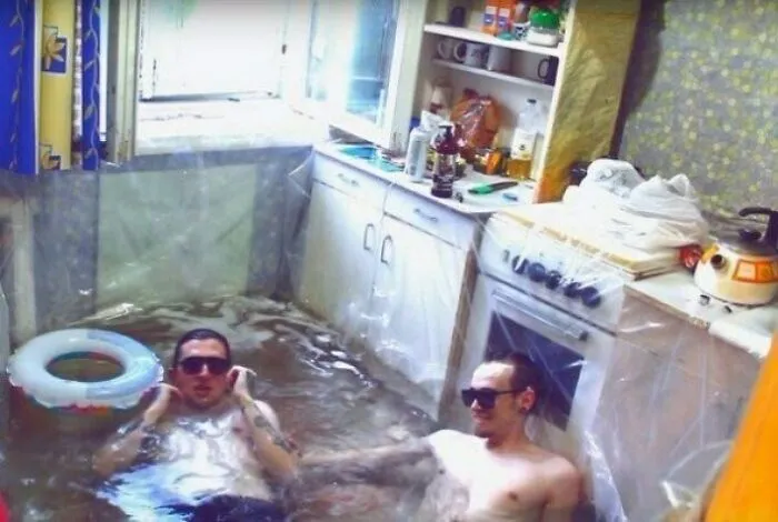 Two men relaxing in a flooded kitchen, showcasing an unhinged image of unexpected leisure.