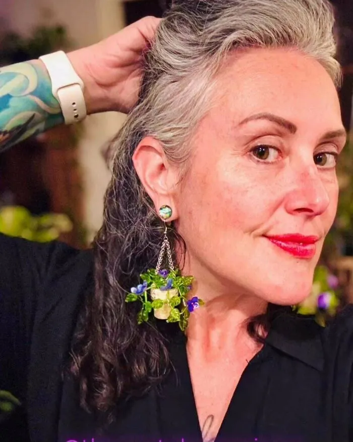 Woman wearing handmade frog-themed earrings with small purple flowers