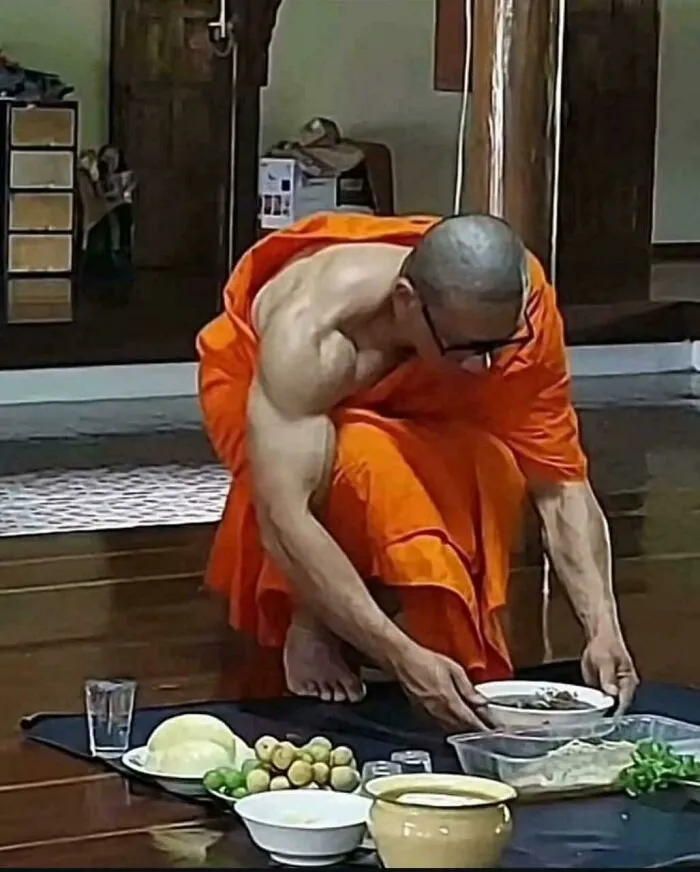 A muscular monk in orange robes bending over food, an unhinged image.