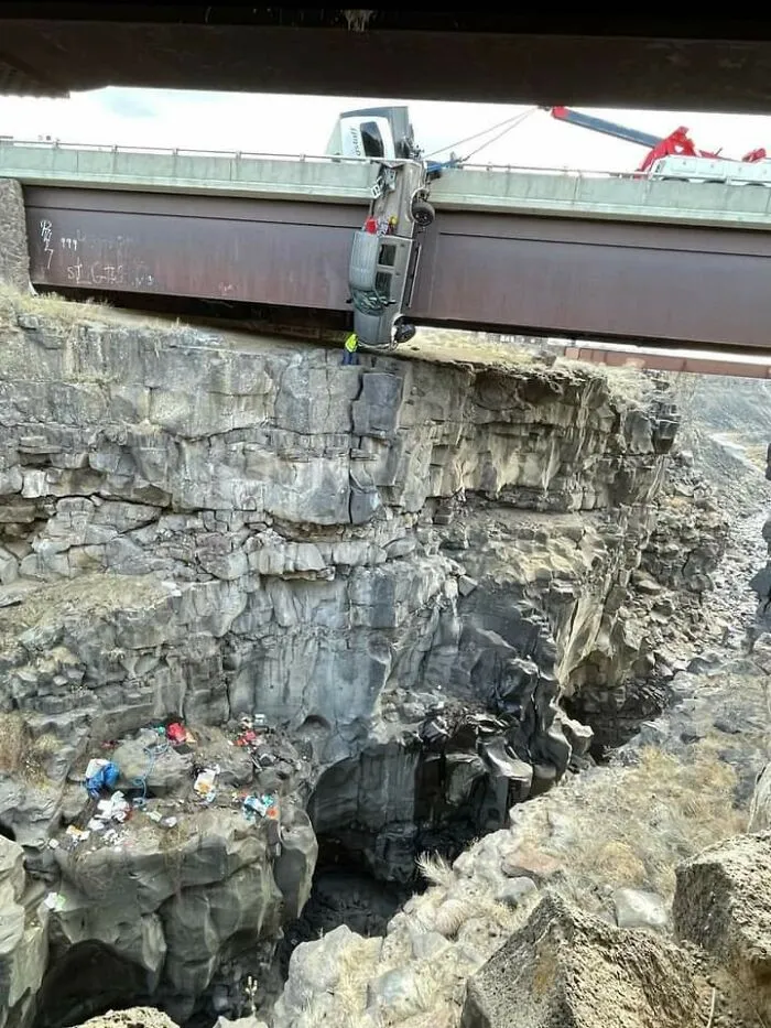 A semi-truck hanging precariously off a bridge over a deep canyon, showcasing an amazing synced moment of peril.