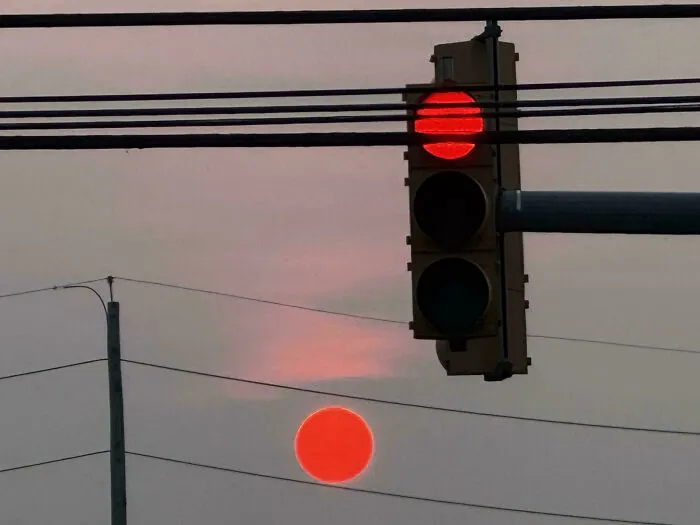 A traffic light with a red stop signal, perfectly synced with the red setting sun below it.