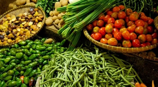A vibrant market stall overflowing with fresh vegetables like peppers, tomatoes, beans, and potatoes. Basic general knowledge quiz.
