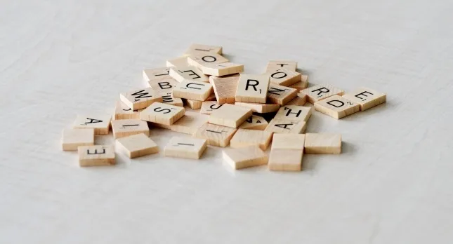 A pile of wooden letter tiles on a light surface. A spelling quiz might use these for word challenges.
