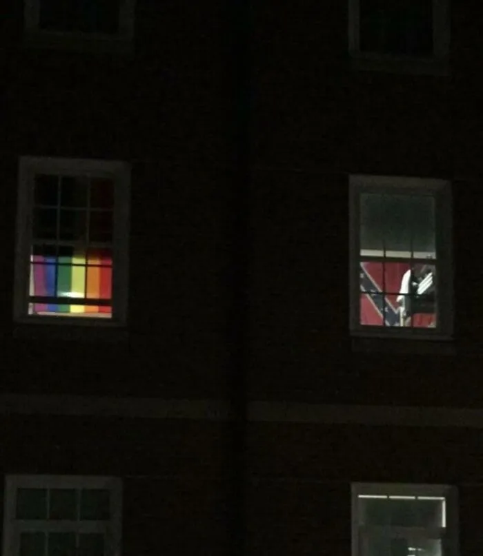 Two unhinged images through windows; one with a pride flag, the other with a Confederate flag.