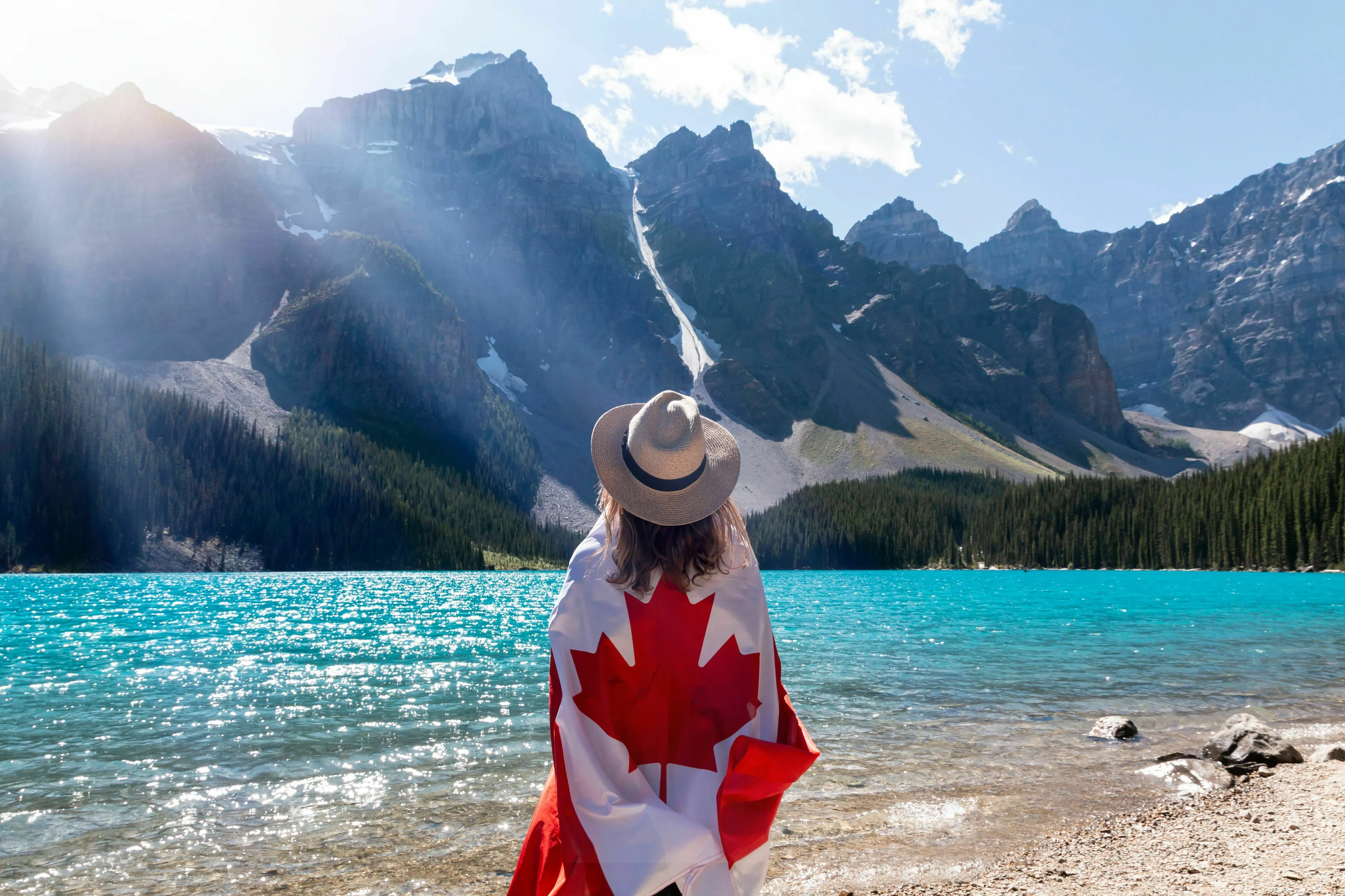 Part 3 General Geography Knowledge Quiz, a person draped in a Canadian flag, looking at a beautiful turquoise lake and mountains.