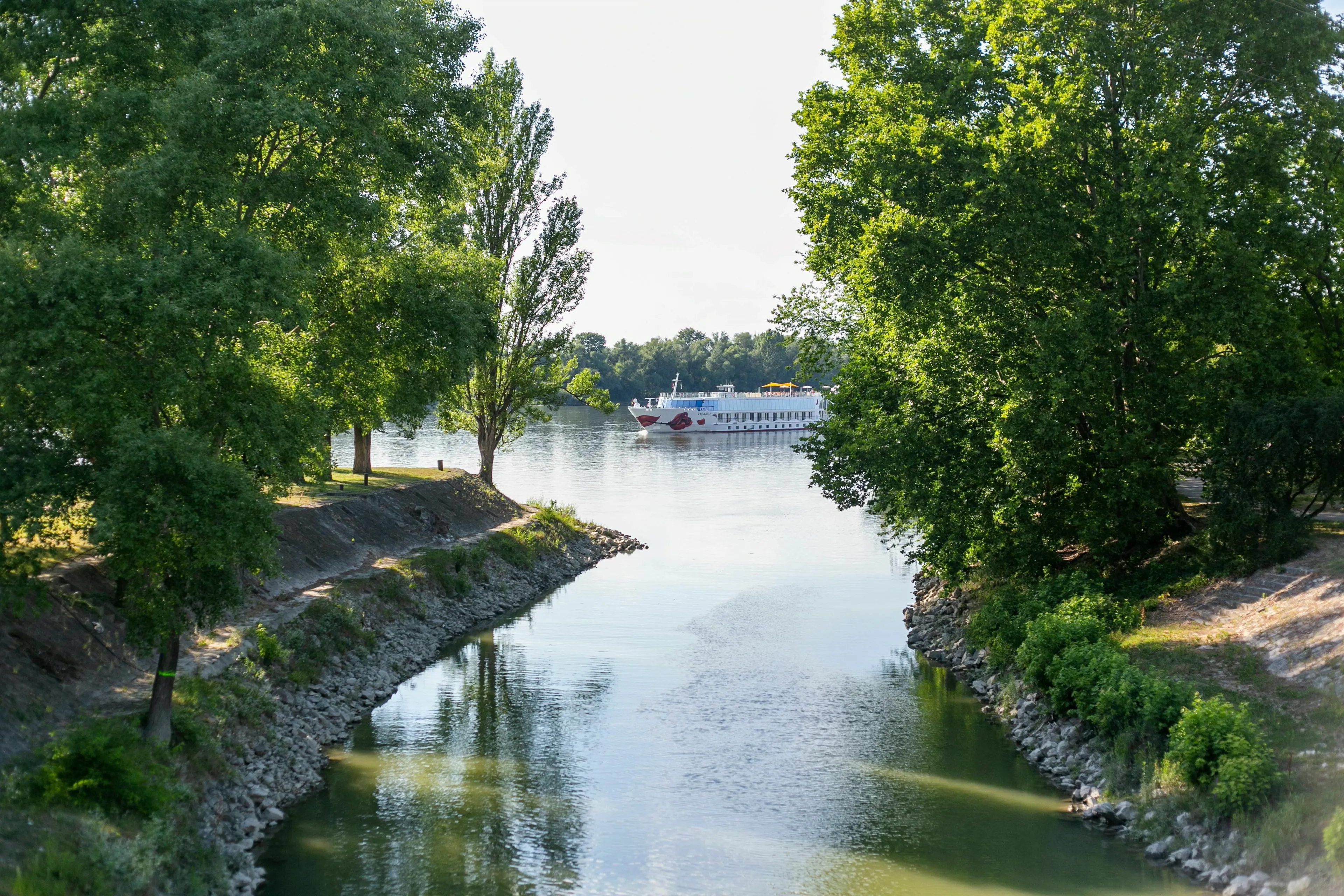 A river flows through Vienna, Budapest, and Belgrade, lined with green trees under a clear sky.